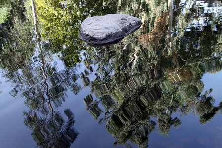 The stone in the pond and the reflection of trees on a background of blue skyの写真素材