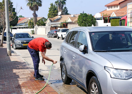 BEER SHEVA, ISRAEL - FEBRUAR 27, 2016: Man washing car from a hose on the street in front of houseのeditorial素材