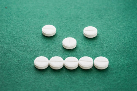 Close-up of white pills forming a neutral face on green backgroundの写真素材