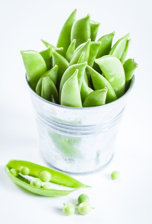 Pods of green peas in a little bucket on a white backgroundの写真素材