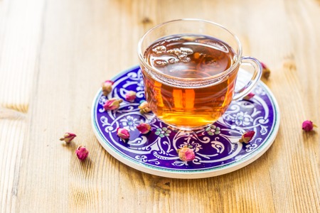 Cup of tea with dry rose buds on wooden tableの写真素材