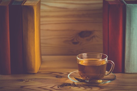 Glass cup with tea and a stack of books with colorful covers. Vintage style filter.の写真素材