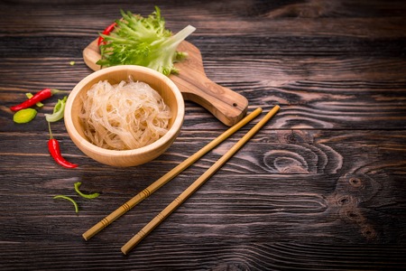 Ingredients of Asian cuisine - rice noodles, leek, lettuce, red hot pepper on a dark wooden backgroundの写真素材