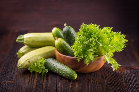 Green cucumbers and salad leaves on a wooden backgroundの写真素材