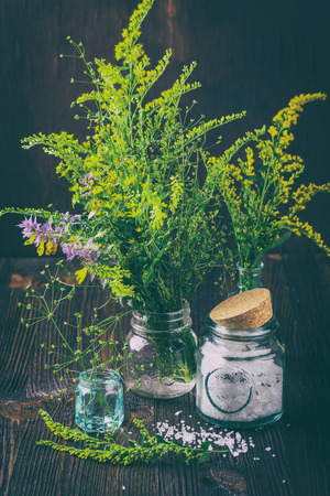 Yellow and purple wild flowers in small glass bottles and jars with cosmetics salt on a wooden tableの写真素材