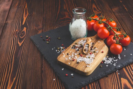 Cherry tomatoes, salt in glass jar, sprinkled with salt and pepper, olive wood spoon on cutting boardの写真素材