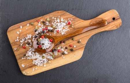 Different types of salt and pepper and scattered wooden spoon on cutting board oliveの写真素材