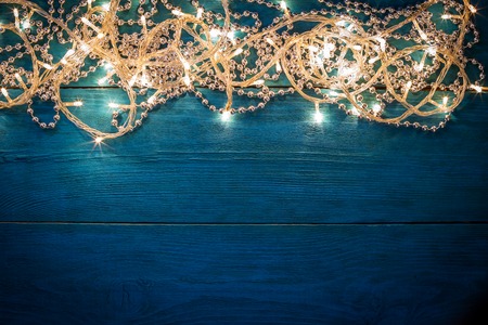 Glowing Christmas garland and silver beads on a blue wooden background. Top view with copy spaceの写真素材