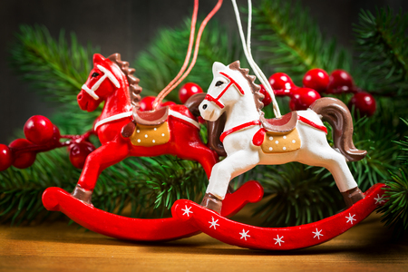 Two Christmas toy horse on a background of branches of Christmas trees and red berriesの写真素材