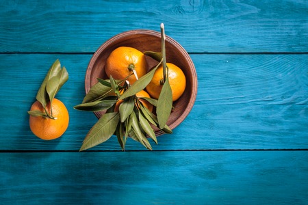Tangerines with leaves in a wooden bowl on blue background. Top view.の写真素材