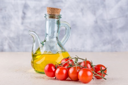 Ingredients for Italian cuisine - a bottle of vegetable oil and cherry tomatoes on a light backgroundの写真素材