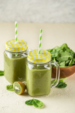 Healthy green smoothies in glass jars and spinach, kiwi ingredients on a light backgroundの写真素材