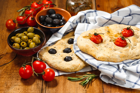 Traditional Italian Focaccia with tomatoes and olives and rosemary with olive oil on wooden tableの写真素材