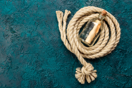 Bottle with a note and a sea rope on a dark turquoise background. Top view. Place for the text.の写真素材