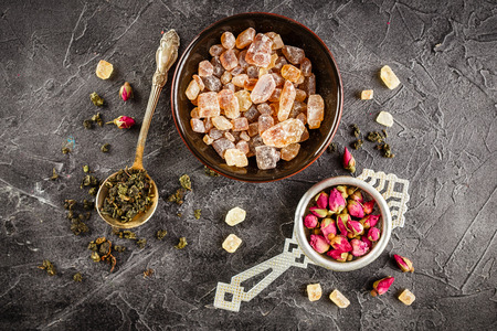 Dry rose buds in a small metal strainer, and dry green tea in the spoon and the bowl of caramelized brown sugar.の写真素材
