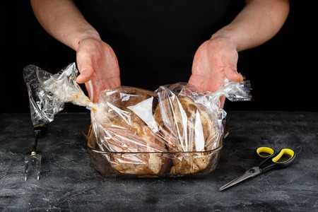 Man stacks marinated meat pieces pork shoulder in the roasting sleeve into glass moldの写真素材