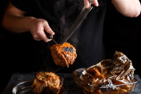 Man takes cooked pieces of marinated pork shoulder from roasting sleeveの写真素材