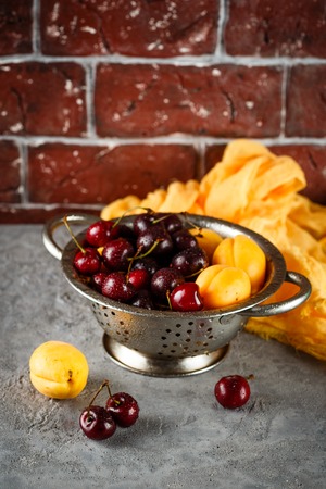 Fresh sweet cherries and apricots in metal colanderの写真素材