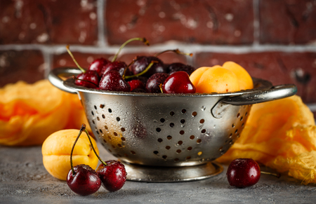 Fresh sweet cherries and apricots in metal colanderの写真素材