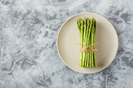 Bundle of raw asparagus on plate on light background. Top viewの写真素材