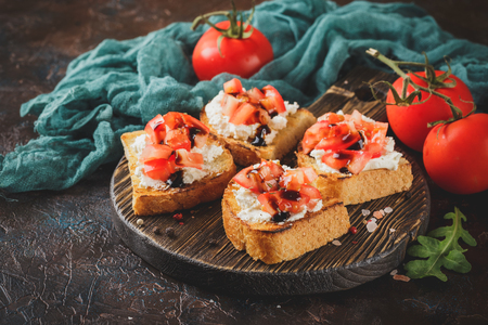 Bruschetta with tomatoes, mascarpone cheese and balsamic sauce on wooden cutting board on dark backgroundの写真素材