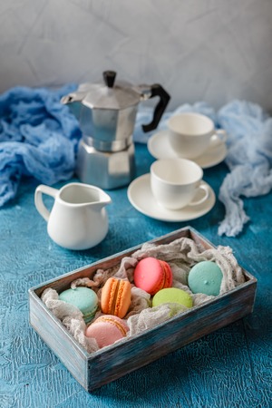 Classic French colorful mackerel cookies in wooden box, cups for coffee and metal coffee maker on blue backgroundの写真素材