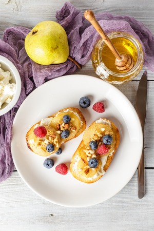 Crostini with ricotta cheese, fried pear, nuts and honey, decorated with raspberries and blueberriesの写真素材