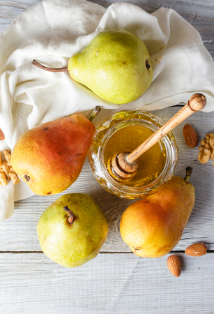 Jar of honey, pears, wooden spoon and walnuts and almonds on light wooden backgroundの写真素材