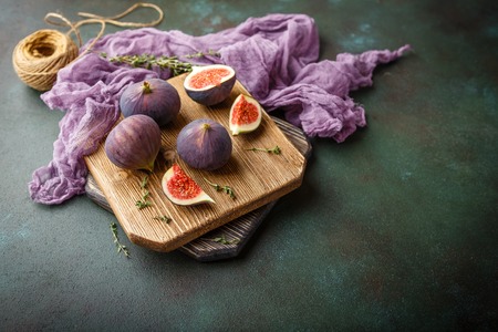 Juicy fresh whole fig fruits and one cut figs on wooden cutting board on dark green backgroundの写真素材