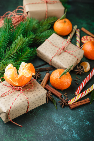 Fresh mandarins with leaves, candy canes, gift boxes in kraft paper and spices - cinnamon, anise and cloves on a dark green backgroundの写真素材