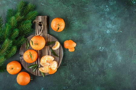 Fresh mandarins with leaves on a dark cutting board on a dark green background. Top viewの写真素材