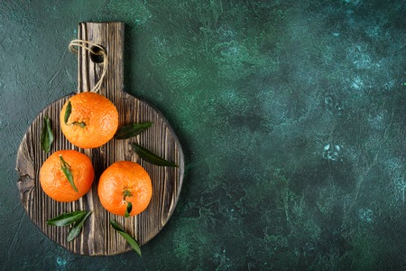Orange tangerines with green leaves on dark wooden board. Top viewの写真素材