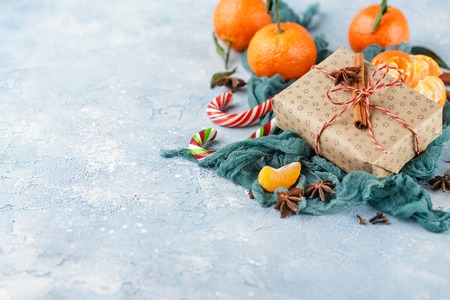 Fresh mandarins with leaves, candy canes, gift boxes in kraft paper and spices - cinnamon, anise and cloves on a blue backgroundの写真素材