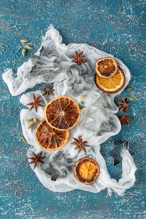 Dried orange slices, cinnamon sticks, anise stars, cardamom seeds in wooden bowls and metal biscuit molds on a blue backgroundの写真素材