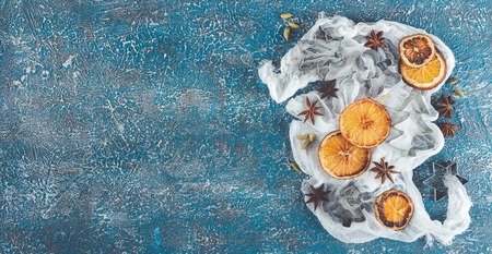 Dried orange slices, cinnamon sticks, anise stars, cardamom seeds in wooden bowls and metal biscuit molds on a blue backgroundの写真素材