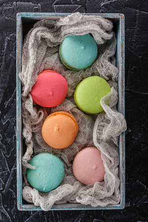 Classic French multicolored macaroon cookies in a wooden box on a black concrete backgroundの写真素材