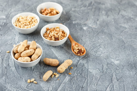 Set of different types of nuts - peanuts in shells, pine nuts and homemade granola on gray...