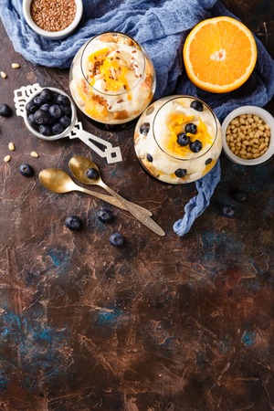 Healthy homemade layered dessert trifle with orange, blueberry, biscuit, yogurt and granola in a glasses. Top view. Place for textの写真素材