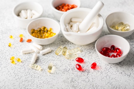 Assorted pharmaceutical medicine pills, tablets and capsules on white bowlsの写真素材