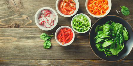 Fresh vegetables and greens on kitchen wooden worktop, top view. Ingredients for salad - spinach, carrots, cucumbers, tomatoes and radish. Healthy eating concept bannerの写真素材