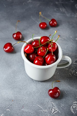 Enameled metal mug with ripe sweet cherries on grey concrete background.の写真素材