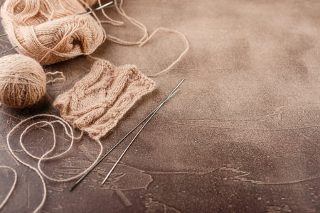 Hanks of woolen brown threads, knitting needles and a knitting pattern on a brown background