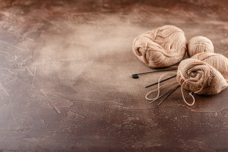 Hanks of woolen brown threads, knitting needles and a knitting pattern on a brown background