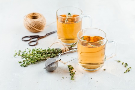 Transparent glasses cup of herbal tea with thyme and sprigs of thyme tied in a bunch on a white backgroundの写真素材