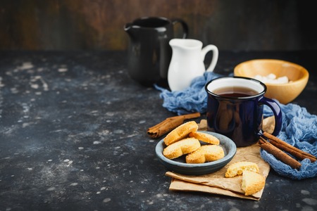 Blue enamelled cup of tea, cinnamon sticks, anise stars and shortbread on a dark background. Space for text.の写真素材