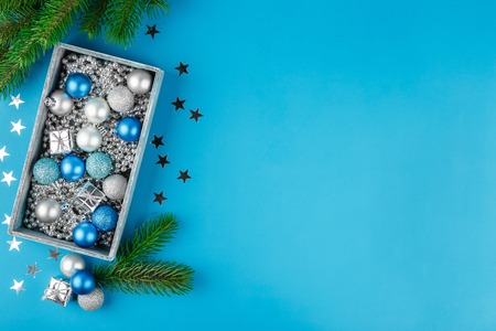 Christmas blue and silver balls, silver Christmas beads in a wooden box on a blue background. Flat lay. Festive border for greeting cardの写真素材