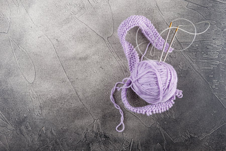 Hanks of woolen lilac threads, knitting needles and a knitting pattern on gray background