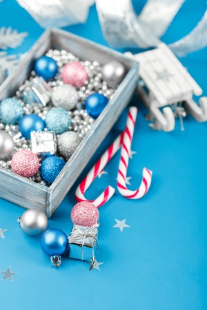 Pink, silver and blue Christmas balls, silver Christmas beads in a wooden box and candy canes on a blue backgroundの写真素材