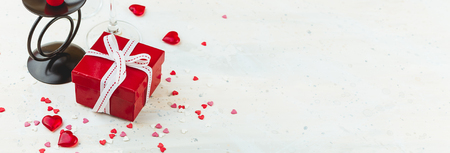 Valentine's day concept, red gift box with white ribbon, wine glass, red candle and hearts jn light background, copy space. Long wide bannerの写真素材