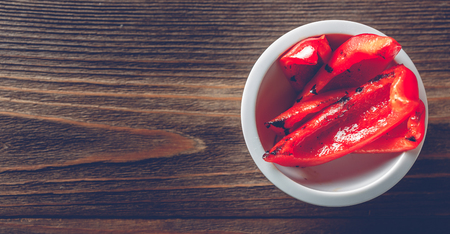 Red grilled bell pepper in white bowl on wooden background. Top view, bannerの写真素材